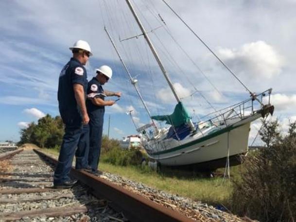 Two people wearing hard hats next to a sail boat on land next to a railroad track